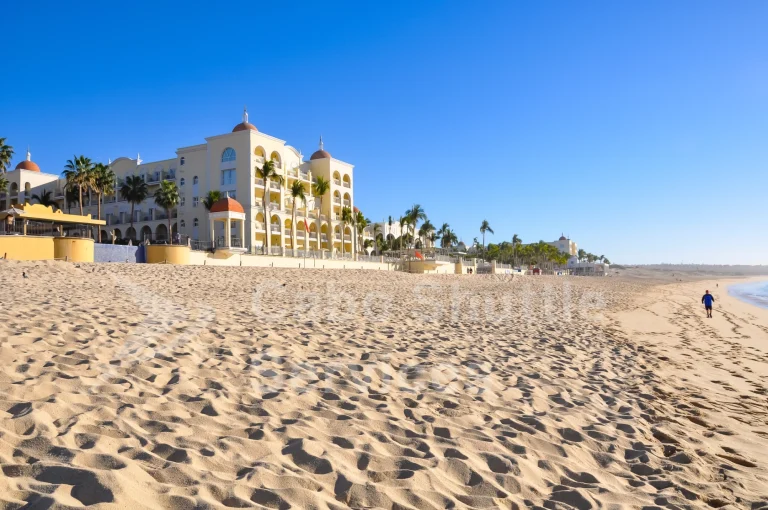 Beachfront view of Riu Palace Cabo San Lucas near Los Cabos Airport with a private shuttle passenger walking along the shore
